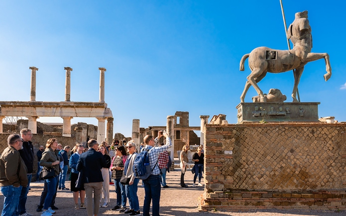Visitors with a guide exploring the ancient ruins of Pompeii with a centaur statue in view.