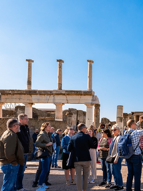 Visitors with a guide exploring the ancient ruins of Pompeii with a centaur statue in view.