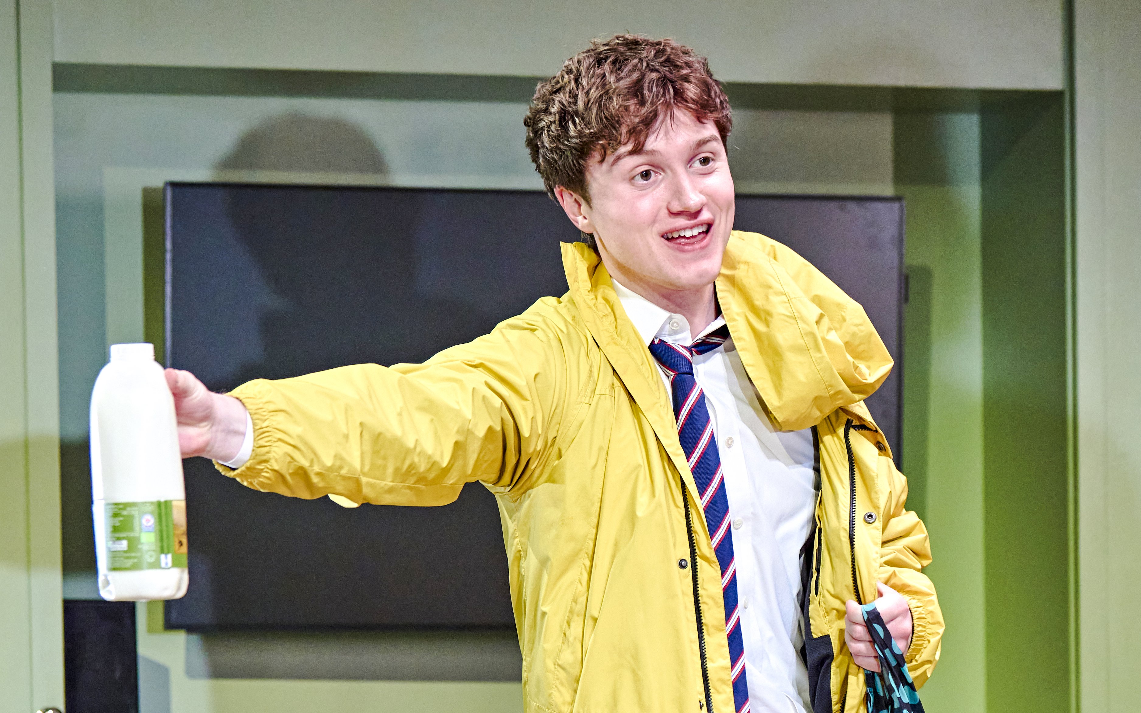 Young man in a yellow jacket holding a milk bottle during Inter Alia production.