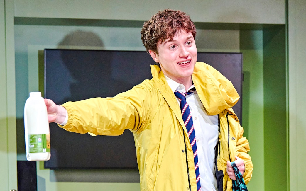 Young man in a yellow jacket holding a milk bottle during Inter Alia production.