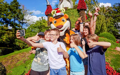 Kids posing with a mascot at an amusement park, giving thumbs up.