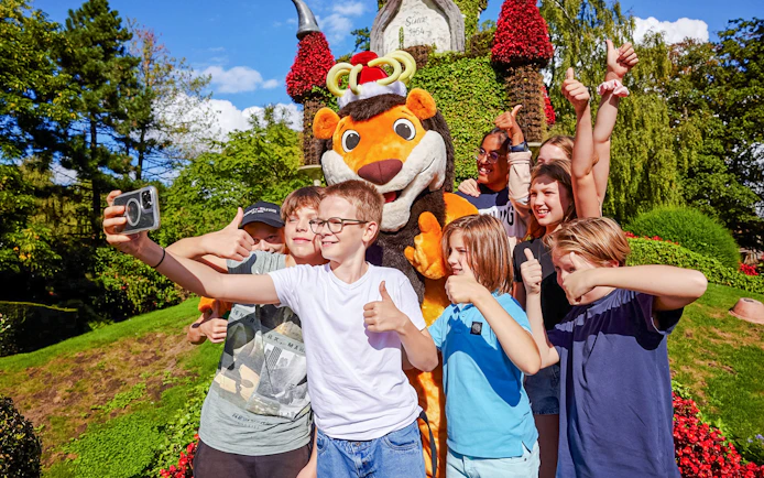 Kids posing with a mascot at an amusement park, giving thumbs up.