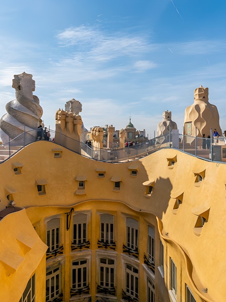La Pedrera rooftop with unique chimneys and Barcelona cityscape in the background.