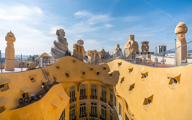 La Pedrera rooftop with unique chimneys and Barcelona cityscape in the background.