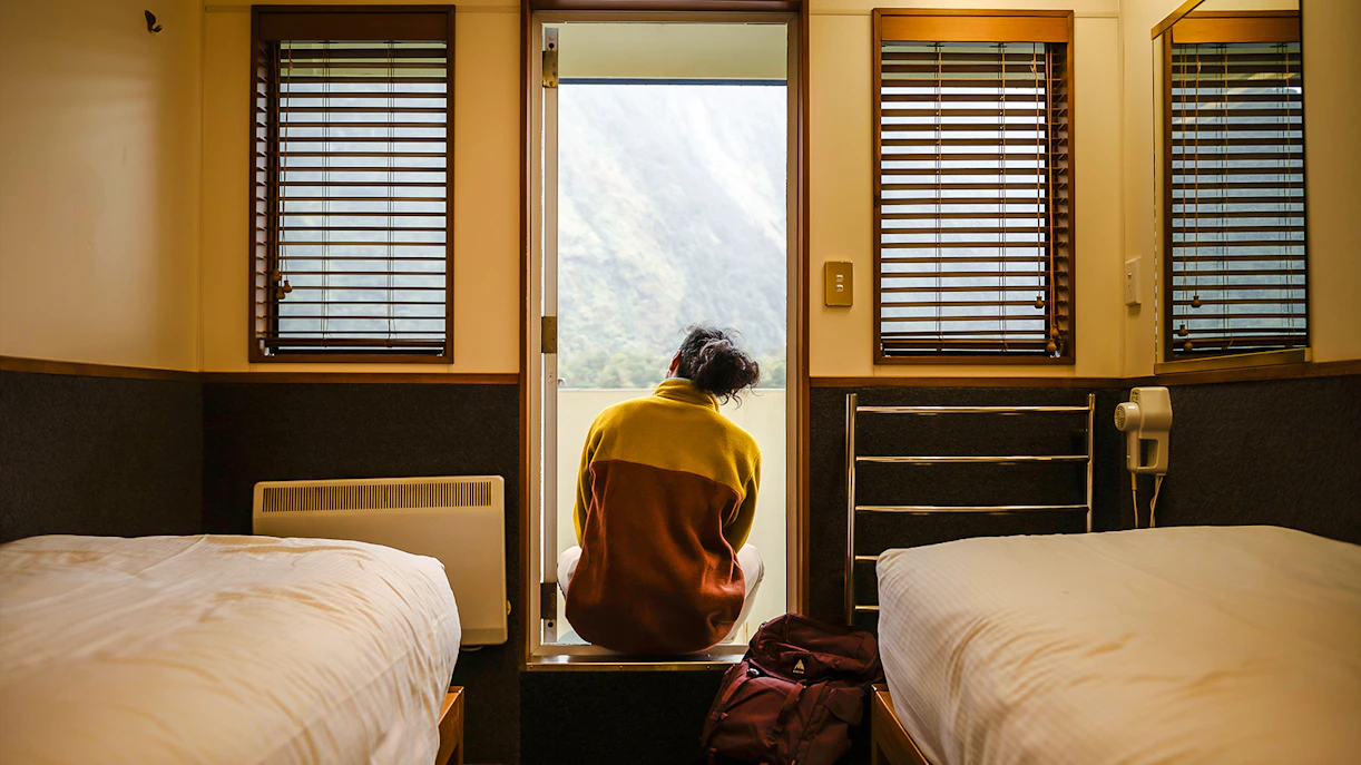 Person sitting in a cabin doorway on a ship, overlooking Milford Sound.
