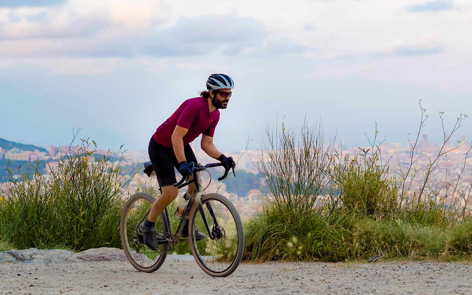Cyclist on mountain road with Barcelona cityscape in background.