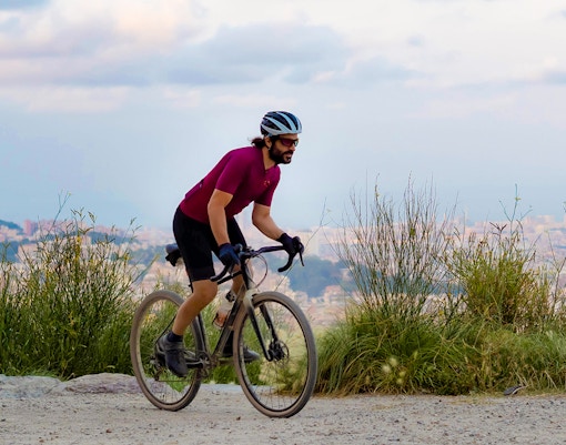 Cyclist on mountain road with Barcelona cityscape in background.