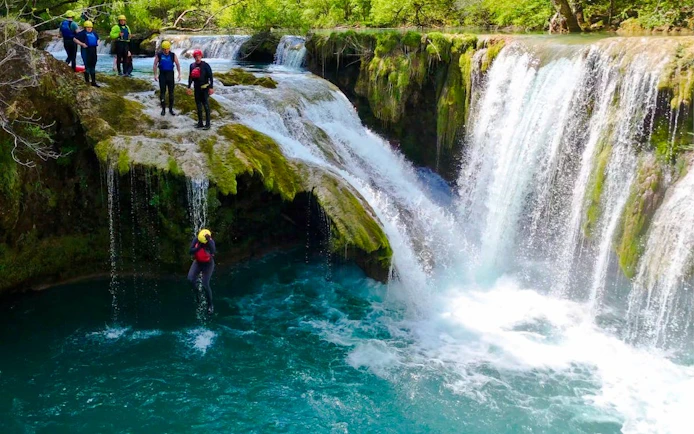 Tourists jumping into Mrežnica Canyon Waterfalls, Split, wearing helmets and life vests.
