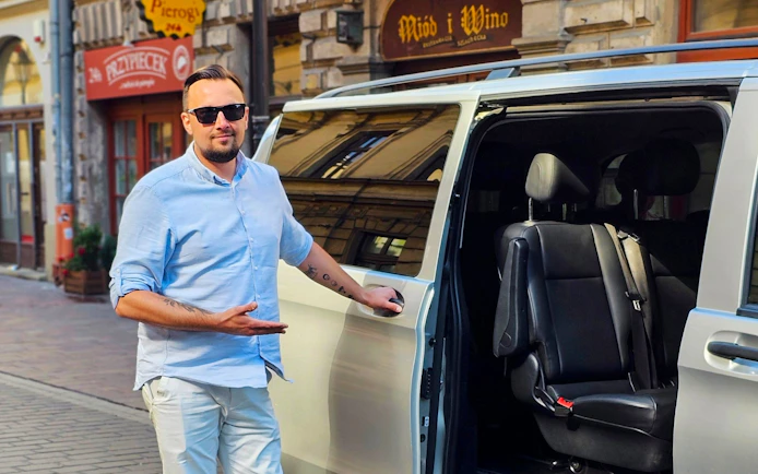 Man standing by an open van door for round-trip AC transfers in Krakow, Poland.