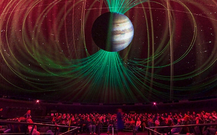 Audience watching cosmic projection in planetarium during space-themed tour.