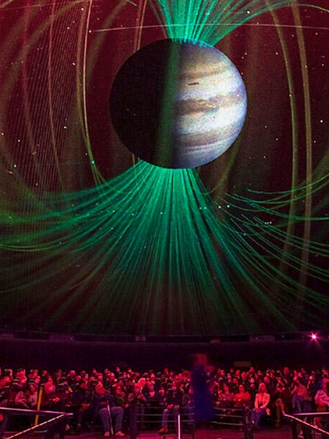 Audience watching cosmic projection in planetarium during space-themed tour.