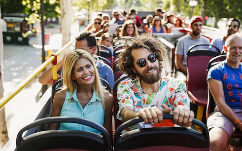 Tourists enjoying a ride on a hop-on hop-off bus in a sunny city.