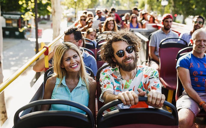 Tourists enjoying a ride on a hop-on hop-off bus in a sunny city.