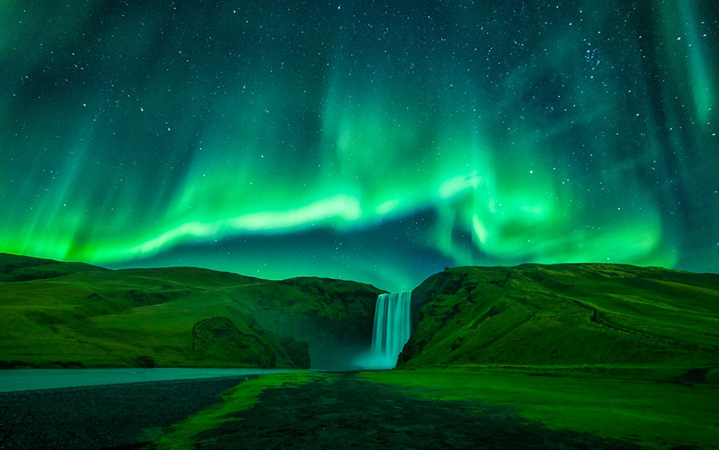 Northern lights over Skógafoss waterfall during Northern Lights Sightseeing Bus Tour.