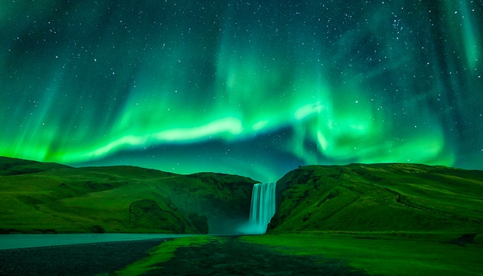 Northern lights over Skógafoss waterfall during Northern Lights Sightseeing Bus Tour.