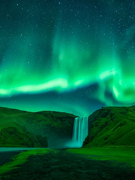 Northern lights over Skógafoss waterfall during Northern Lights Sightseeing Bus Tour.