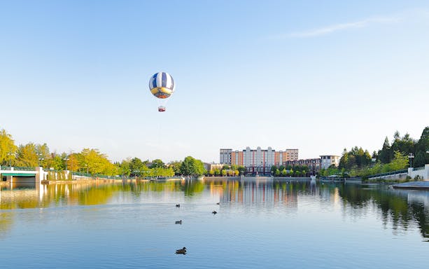 Ballon Panoramagique floating over a lake with buildings and trees in the background.