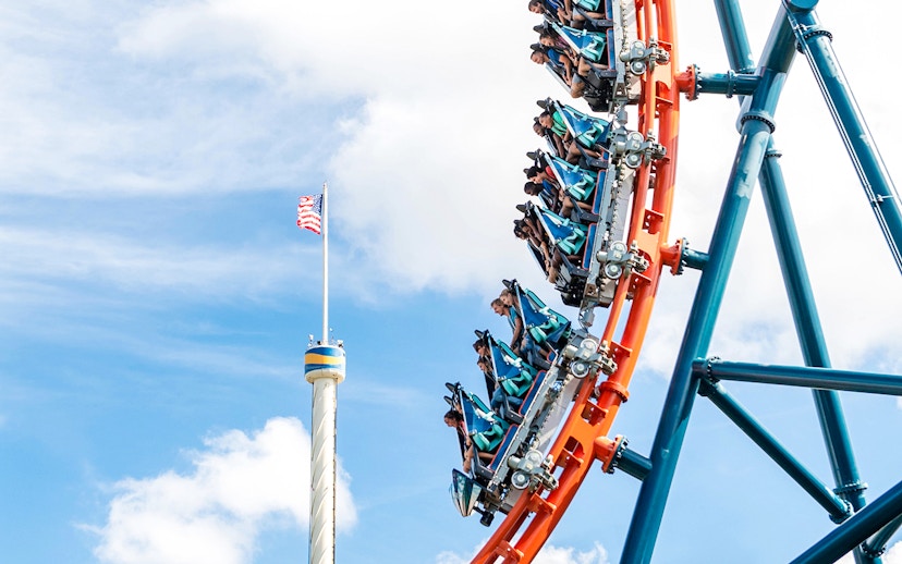 Riders on Ice Breaker roller coaster at SeaWorld Orlando with American flag in background.