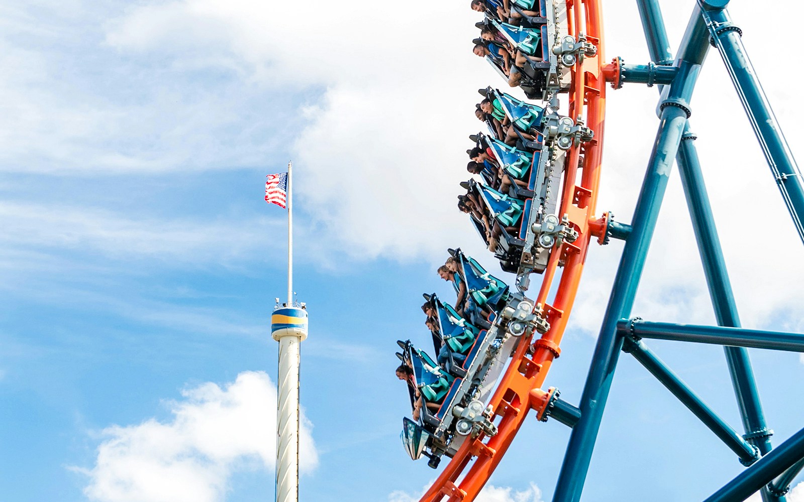 Riders on Ice Breaker roller coaster at SeaWorld Orlando with American flag in background.