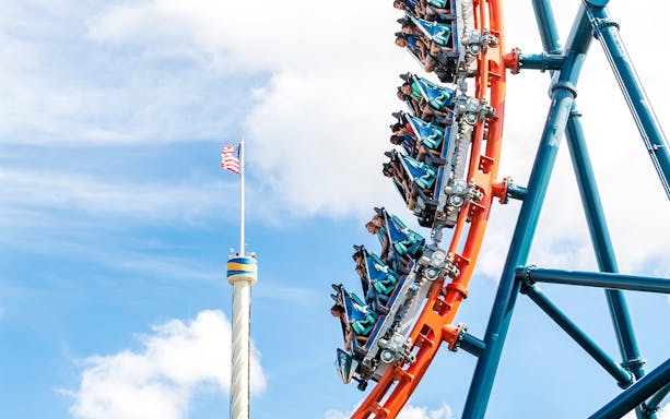 Riders on Ice Breaker roller coaster at SeaWorld Orlando with American flag in background.