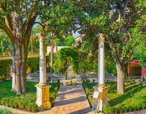 The Dance's Garden fountain in Royal Alcazar Garden, Seville, Spain, surrounded by lush greenery.