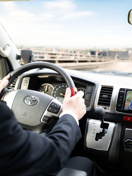 Driver navigating Kansai Airport shared shuttle van with GPS, heading towards hotel drop-off.