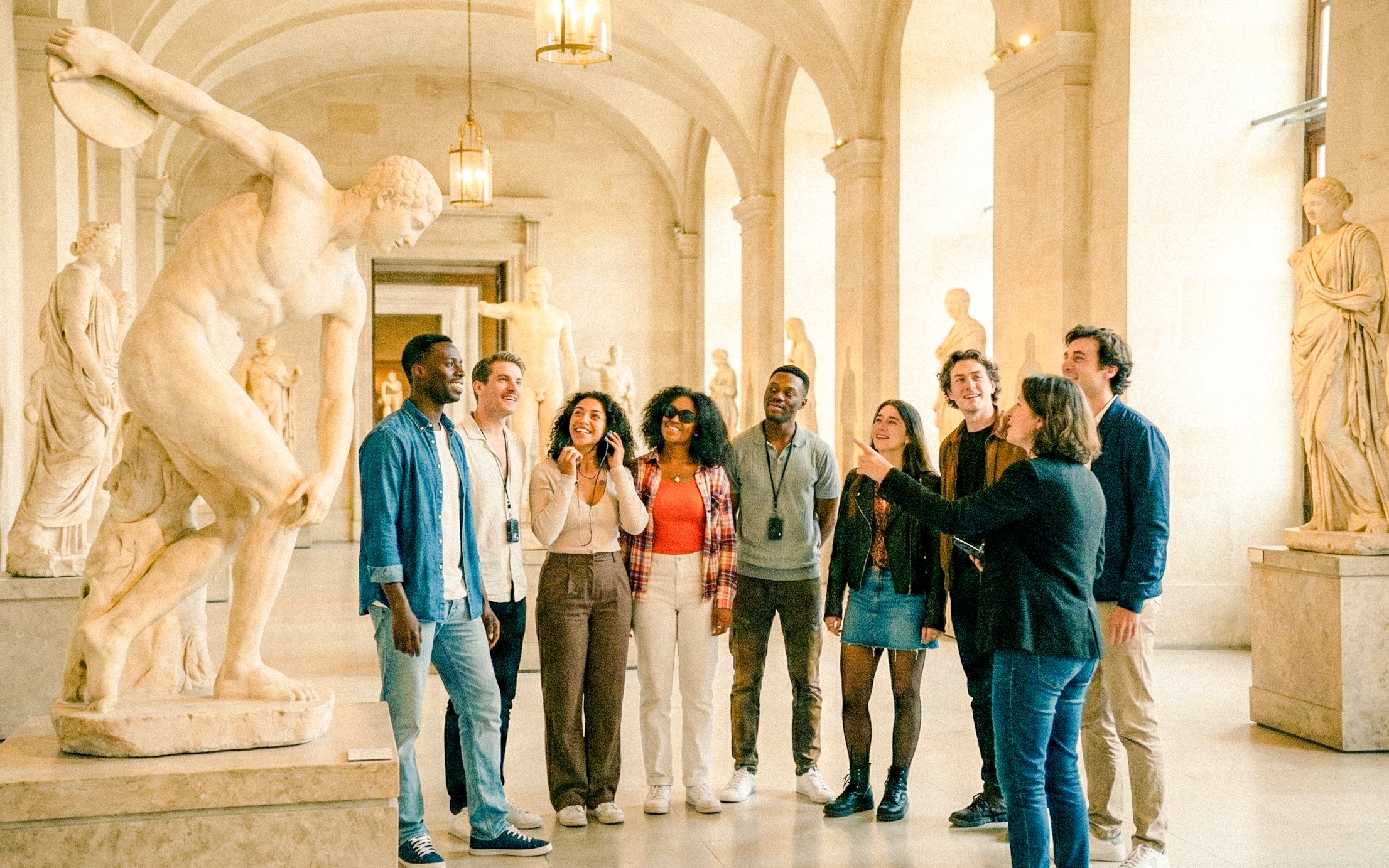 Tour group with guide in Louvre Museum, Paris, viewing classical sculptures.