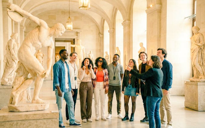 Tour group with guide in Louvre Museum, Paris, viewing classical sculptures.