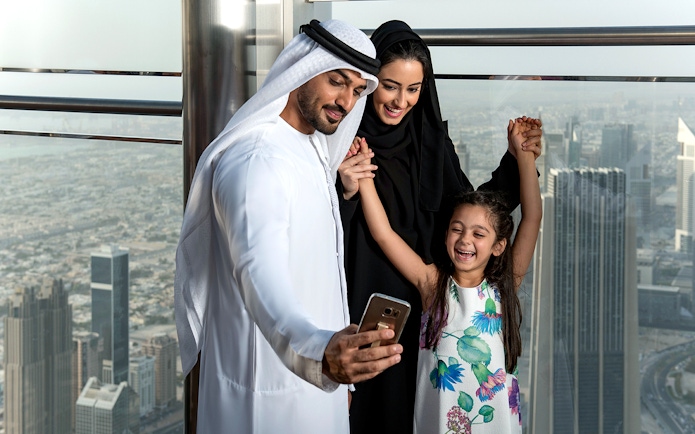 Family taking a selfie at Burj Khalifa observation deck, Dubai skyline in background.