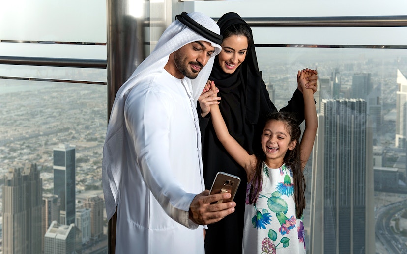 Family taking a selfie at Burj Khalifa observation deck, Dubai skyline in background.