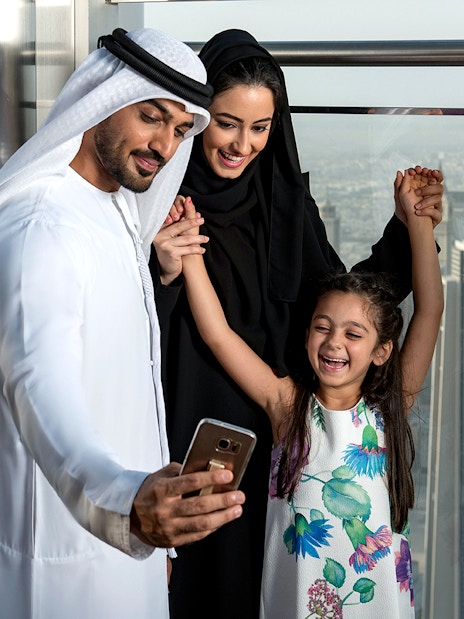 Family taking a selfie at Burj Khalifa observation deck, Dubai skyline in background.
