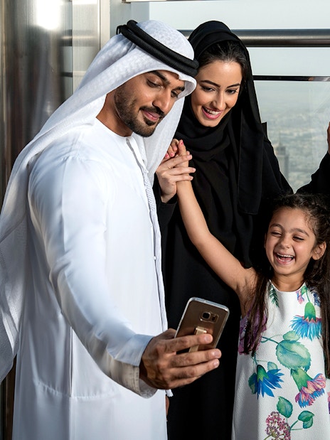 Family taking a selfie at Burj Khalifa observation deck, Dubai skyline in background.