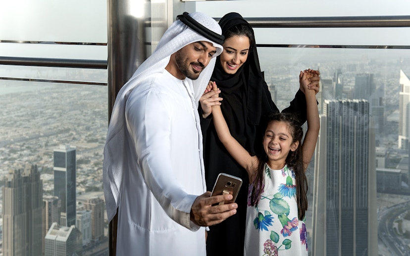 Family taking a selfie at Burj Khalifa observation deck, Dubai skyline in background.