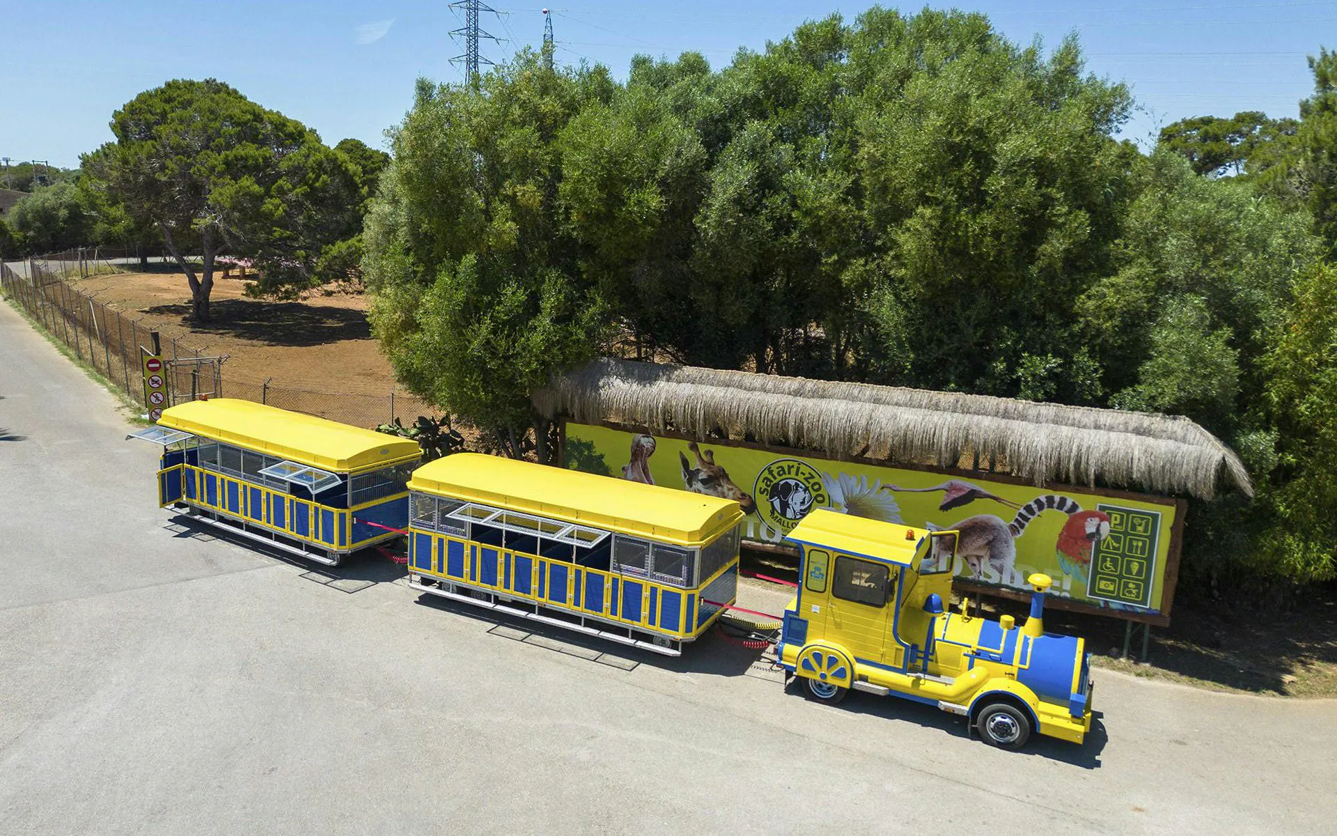 Safari zoo train at Mallorca with yellow and blue carriages near animal mural.