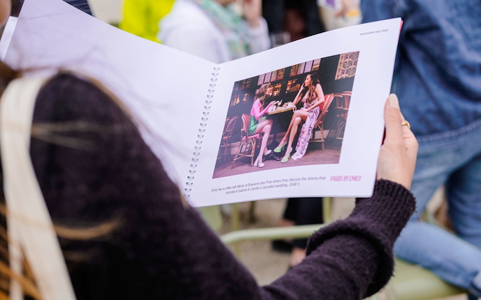 Person holding a booklet with a scene from Emily in Paris during a food tour.