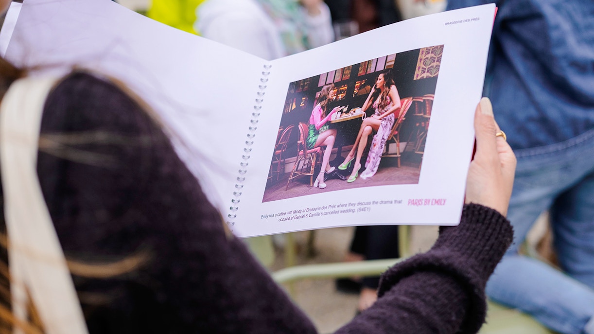 Person holding a booklet with a scene from Emily in Paris during a food tour.