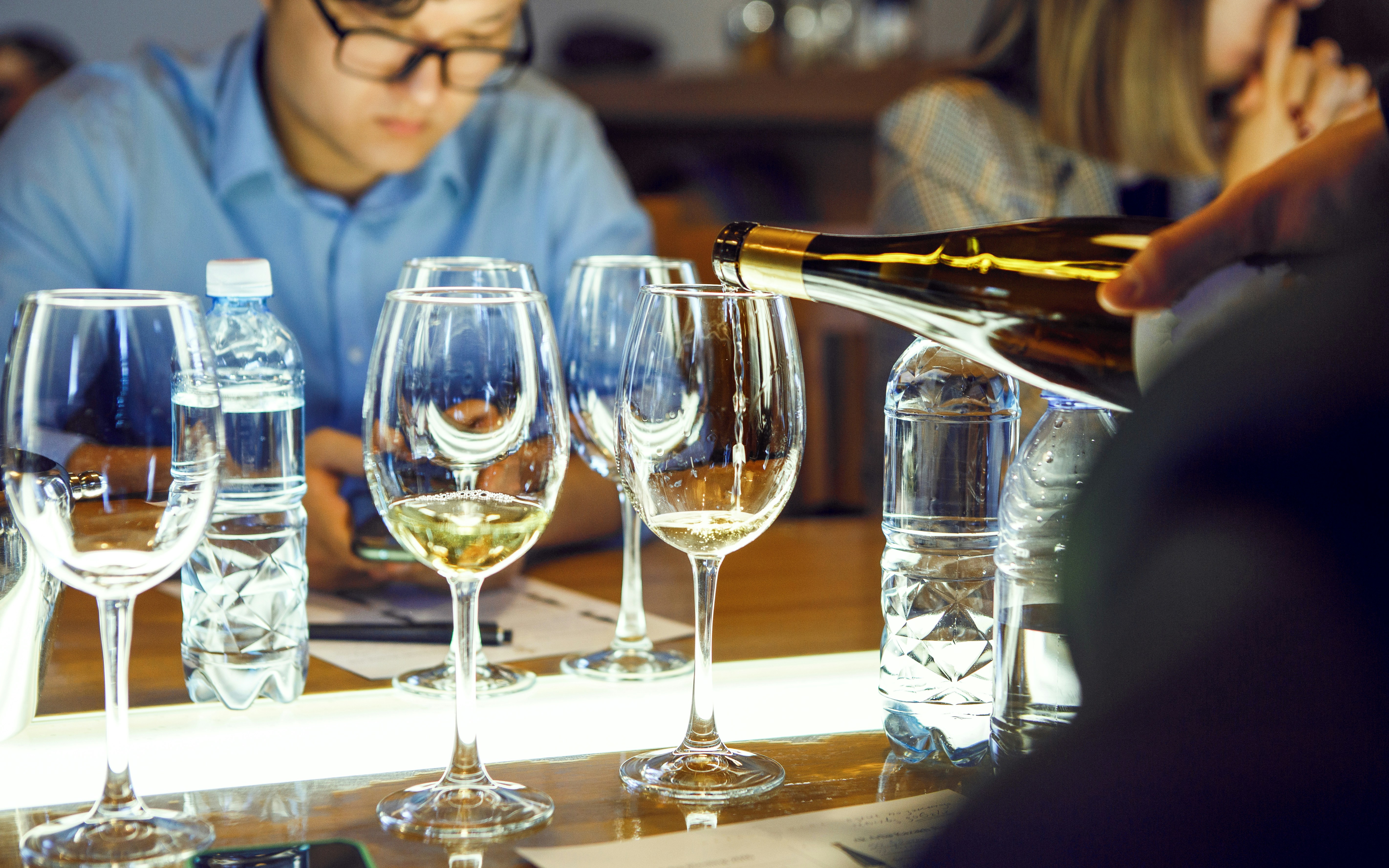 Man pouring wine into glasses during sommelier course.