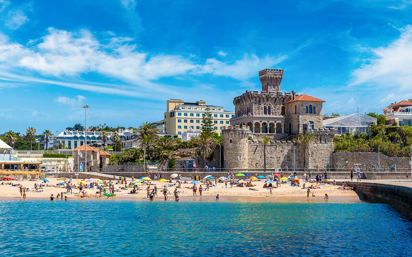 Beachgoers at Cascais with historic castle and buildings in the background, part of Lisbon tour.