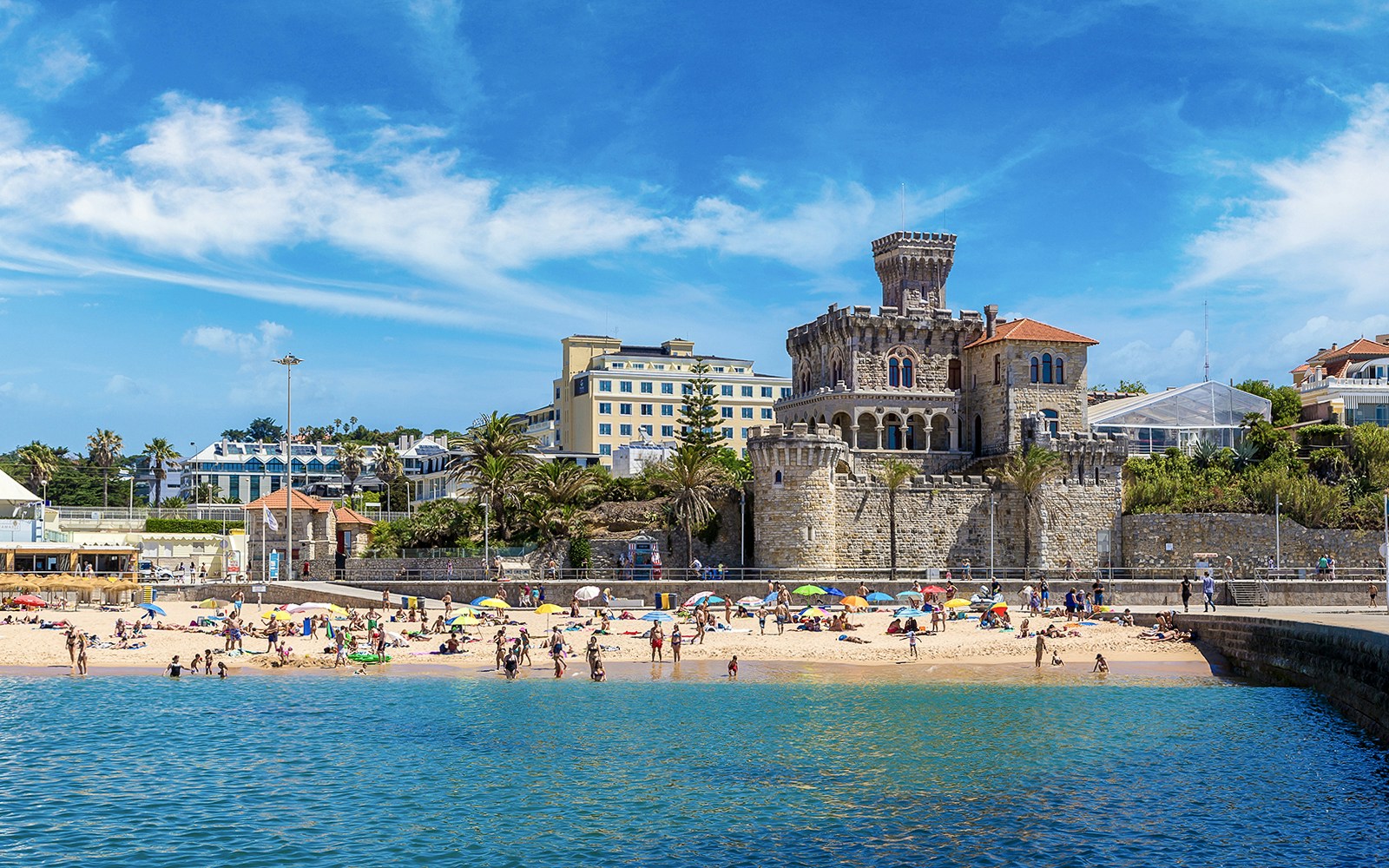 Beachgoers at Cascais with historic castle and buildings in the background, part of Lisbon tour.