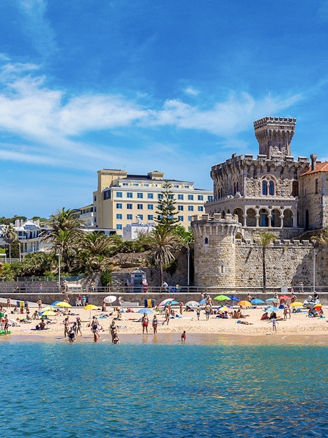 Beachgoers at Cascais with historic castle and buildings in the background, part of Lisbon tour.