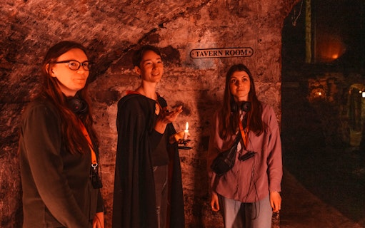 Guests with guide holding candle in Blair Street Underground Vaults' Tavern Room.