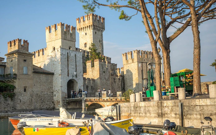 Scaliger Castle in Sirmione with boats docked nearby, part of a full-day tour from Verona.