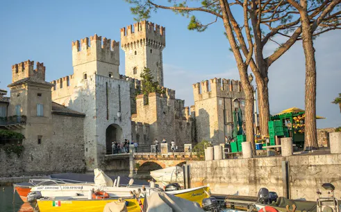Scaliger Castle in Sirmione with boats docked nearby, part of a full-day tour from Verona.