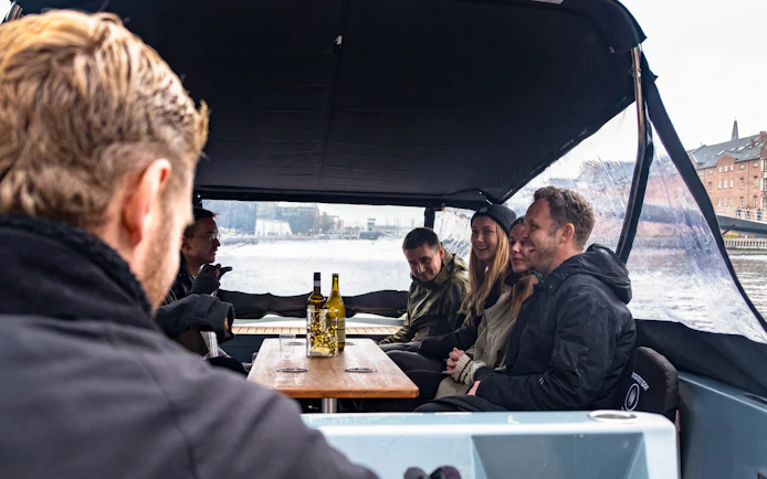 Group enjoying canal cruise on covered boat with city view.