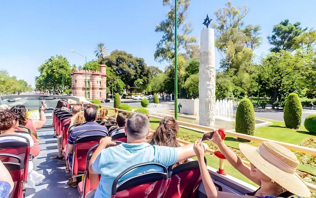Passengers on a hop-on hop-off tour bus in Seville, viewing city landmarks.