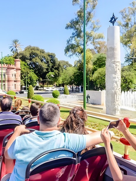 Passengers on a hop-on hop-off tour bus in Seville, viewing city landmarks.