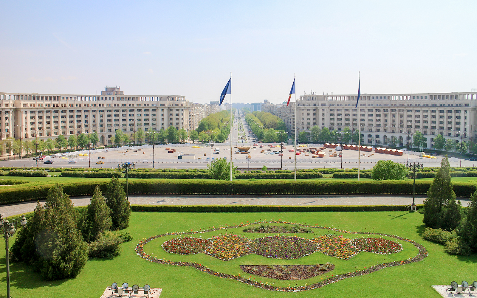 Unirii Boulevard view from Palace of the Parliament, Bucharest, with symmetrical gardens and flags.