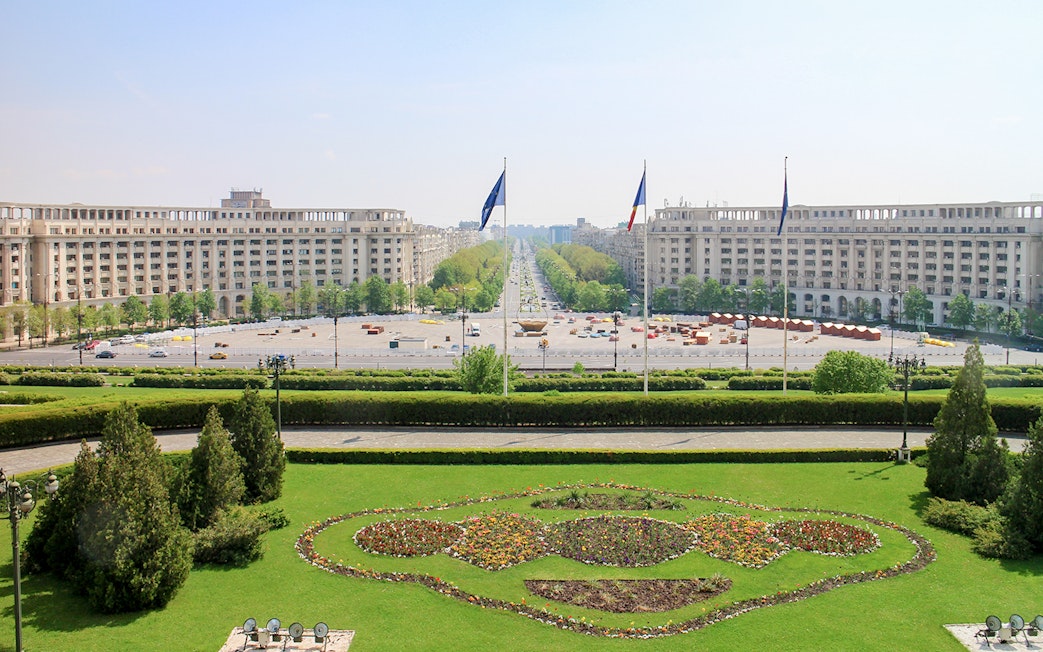 Unirii Boulevard view from Palace of the Parliament, Bucharest, with symmetrical gardens and flags.
