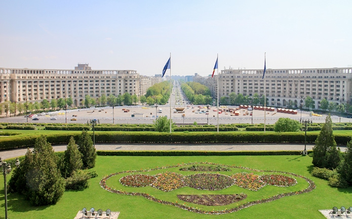 Unirii Boulevard view from Palace of the Parliament, Bucharest, with symmetrical gardens and flags.