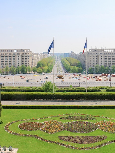 Unirii Boulevard view from Palace of the Parliament, Bucharest, with symmetrical gardens and flags.
